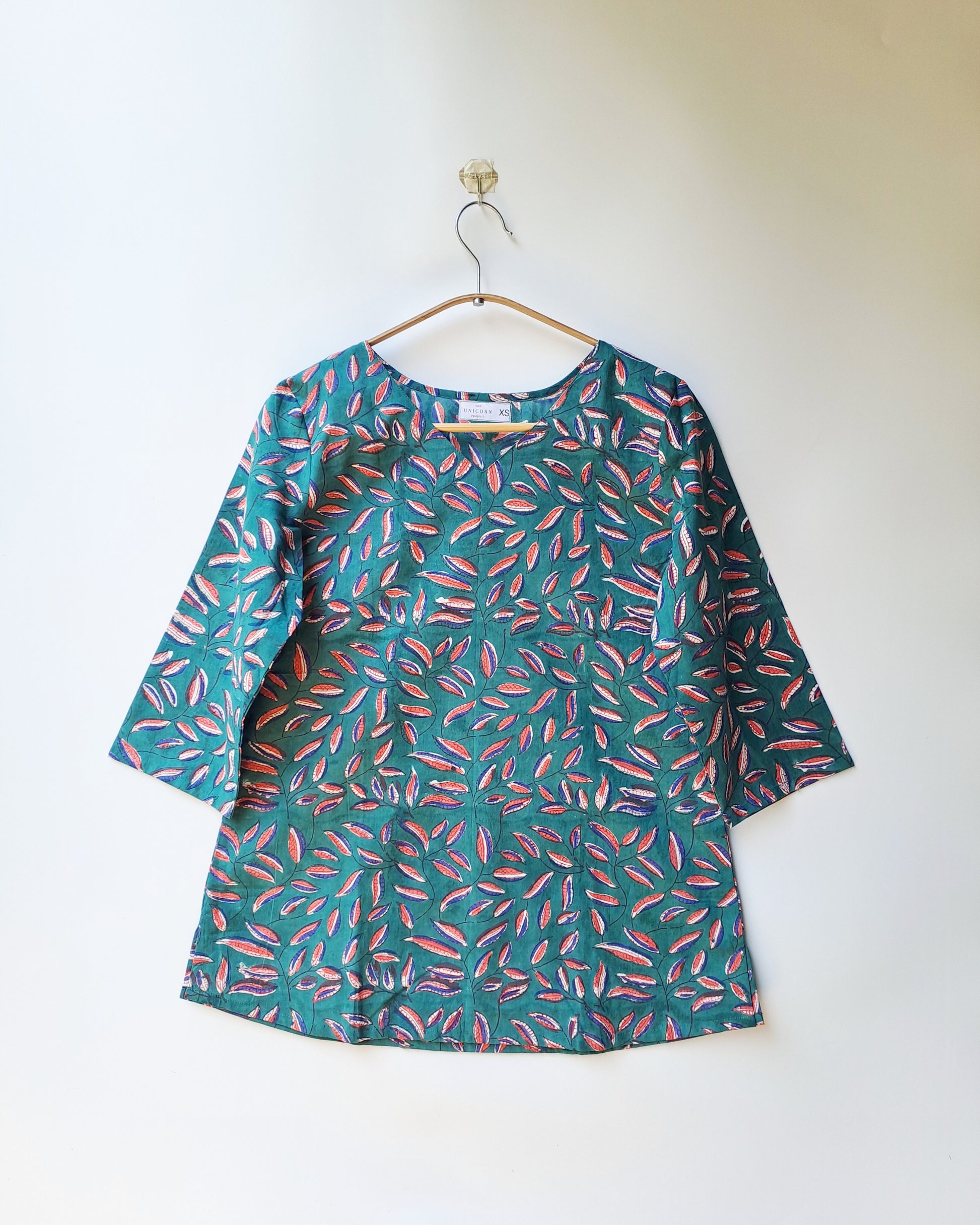 Green dress with pink leaf pattern on a hanger against a white background
